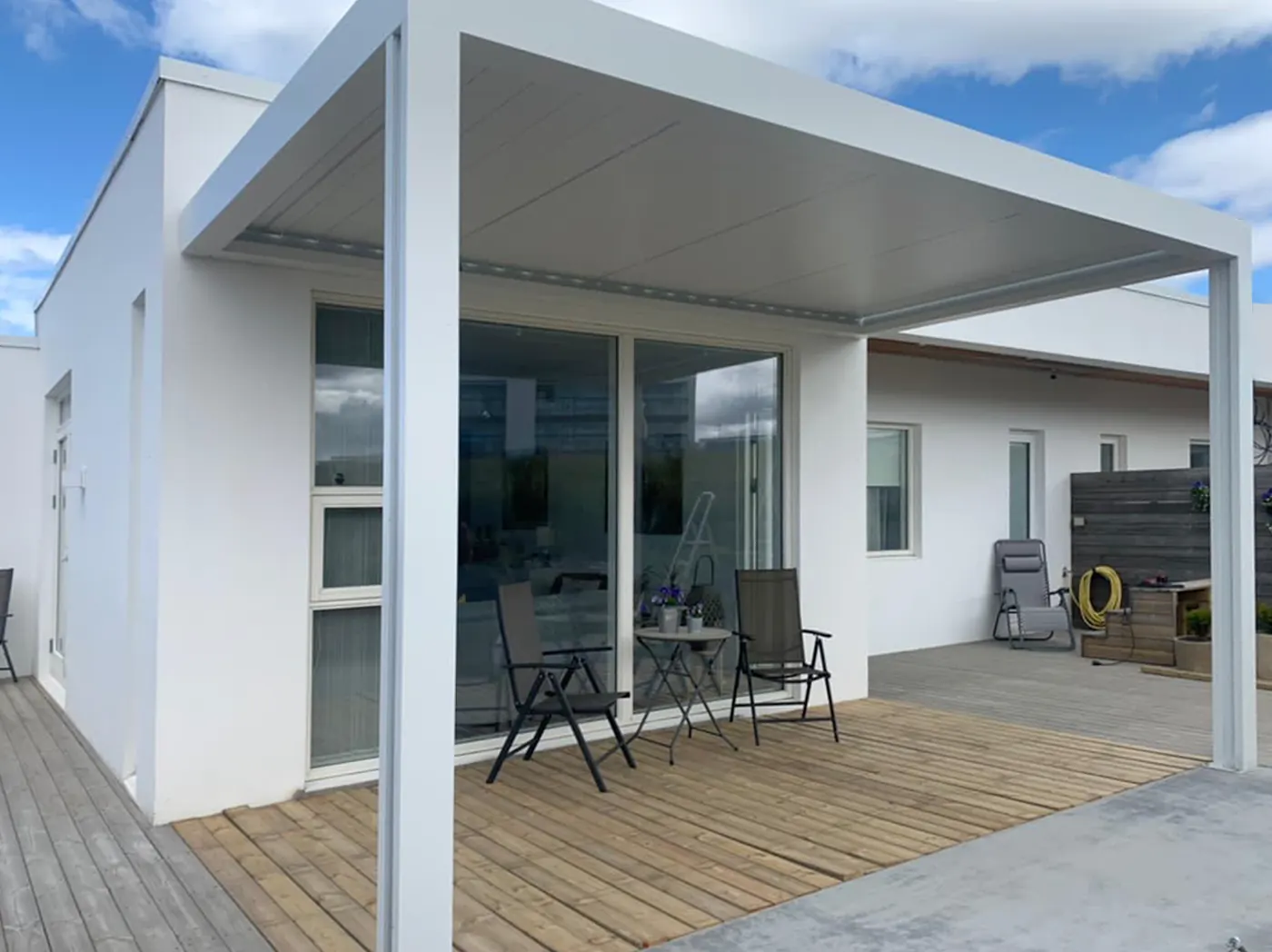 Pergola bioclimatique blanche adossée à une maison, terrasse en bois