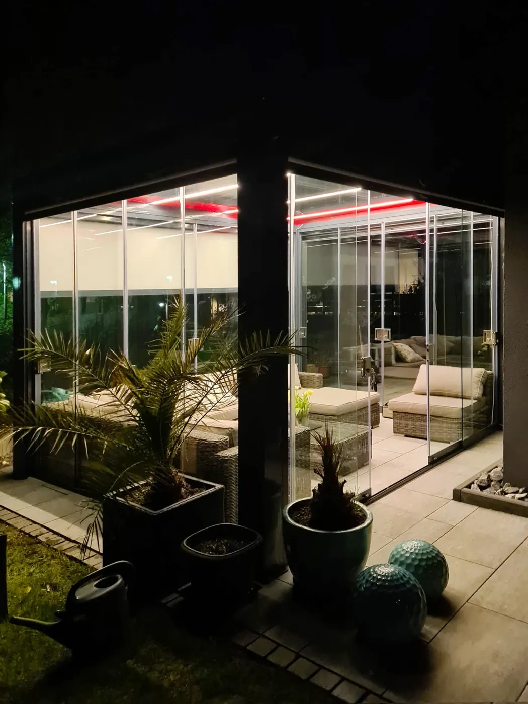 Pergola bioclimatique vitrée éclairée de nuit, plantes et salon