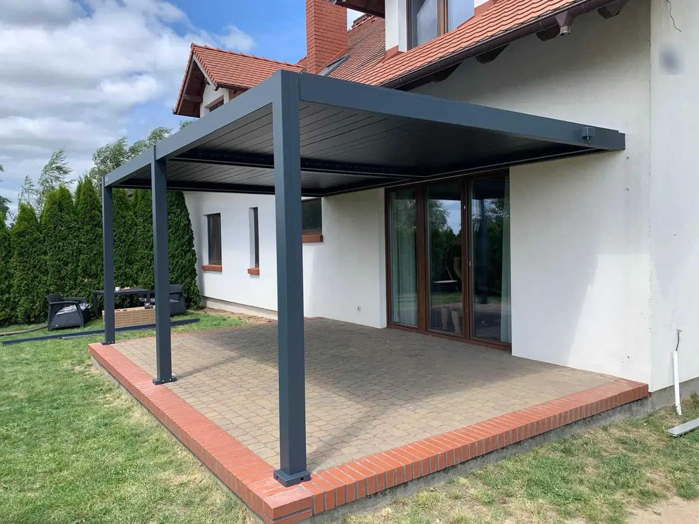 Pergola bioclimatique adossée sur une terrasse bordée de brique